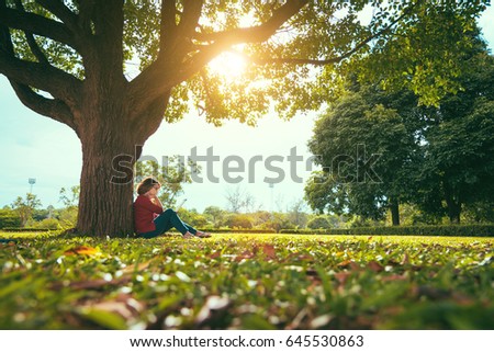 Student woman wearing glasses make a note of something under a tree in the evening with the sun light in selective focus.
