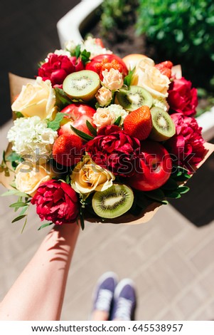 An unusual bouquet of peonies, roses, strawberries, kiwi and apples in hand. Top view. Close up