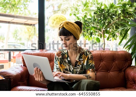 Pretty brunette girl checks her mail on small portable laptop while waiting her order in cafe shop. She travels during her summer vacations and sometimes works remotely Royalty-Free Stock Photo #645550855