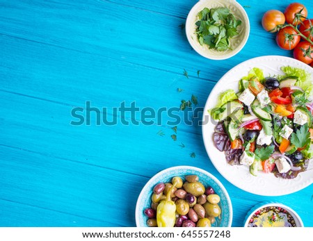 Greek salad background. Bowl with fresh greek salad, tomatoes, olives, olive oil on wooden table. Space for text. Top view. Traditional greek dish. Ingredients for making salad. Mediterranean diet