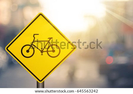 Bicycle warning sign on blur traffic road with colorful bokeh light abstract background. Copy space of transportation and travel concept. Retro tone filter effect color style.