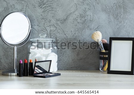 Cotton jar, mirror, empty photo frame and colorful cosmetics