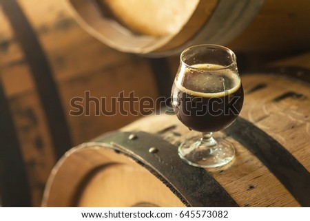 Glass of dark stout beer standing on an oak wood barrel in a brewery Royalty-Free Stock Photo #645573082