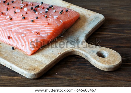 Fresh salmon fillet with aromatic herbs, spices on cutting board on wooden background. Top view. Closeup.