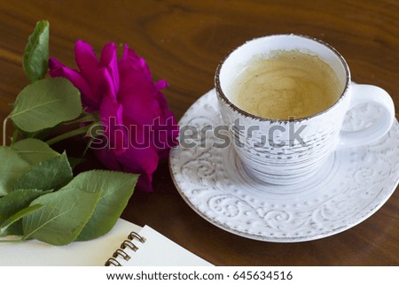 a cup of coffee with notebook and beautiful roses on a wooden table 