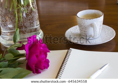a cup of coffee with notebook and beautiful roses on a wooden table 