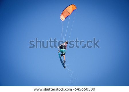 Professional kite boarding rider sportsman with kite in sky jumps high acrobatics kiteboarding trick with grab of kiteboard and huge water splash. Recreational activity, extreme active air sports