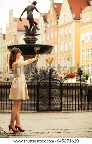 Traveler woman fashion girl taking self picture selfie with smartphone camera outdoors in european city old town Gdansk. Neptune fountain Poland