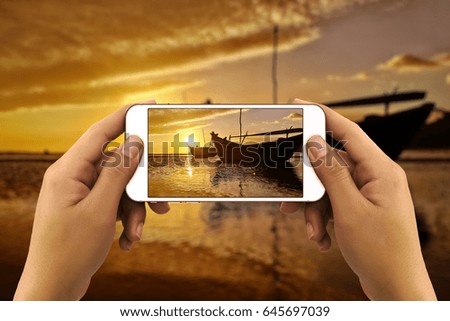 Hands taking photo of sea sunset landscape with fishing boats by smartphone