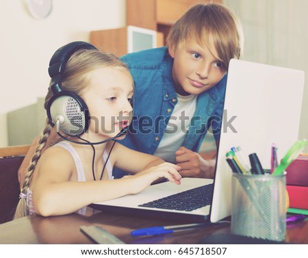 Portrait of smiling little brother and sister busy with online game on laptop
