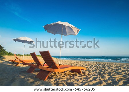 Orange beach chairs and parasols on sandy beach with cloudy blue sky and sea
