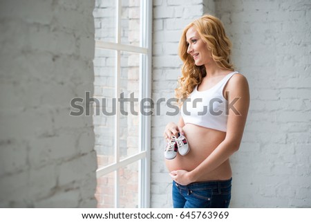 Beautiful red-haired pregnant girl with baby sneakers.