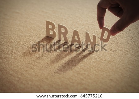 BRAND wood word on compressed or corkboard with human's finger at D letter. Royalty-Free Stock Photo #645775210