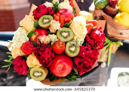 An unusual bouquet of peonies, roses, strawberries, kiwi and apples on blue background. 