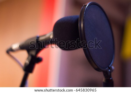 Close up studio condenser microphone with pop filter recording with color lights background. 