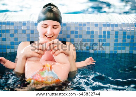 Young mother, swimming instructor and happy little girl in the pool. Teaches infant child to swim. Enjoy the first day of swimming in the water. Mom holds child preparing for diving. doing exercises