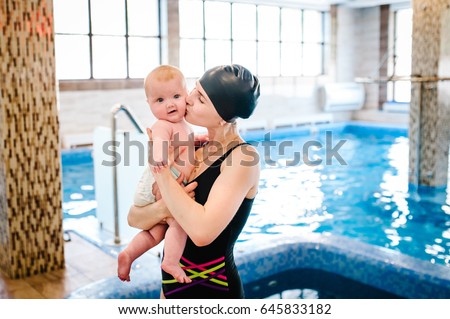 Beautiful mother holding a baby girl 6 months, a baby in her arms at the pool. The first swimming lesson. Mom kissing baby. A child with pleasure by the pool. Pool building