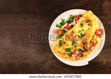 A photo of an omelette with cherry tomatoes, parsley. and grated cheese, shot from above on a rustic wooden texture with a place for text Royalty-Free Stock Photo #645857881