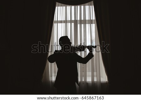Man playing on violin near window. Silhouette. 