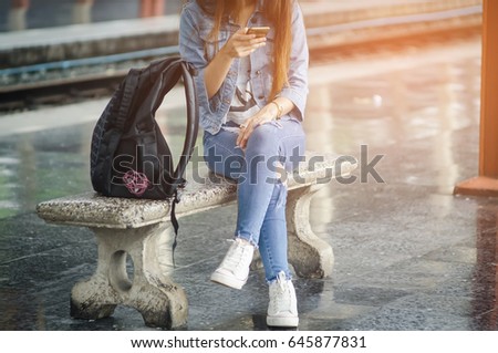 Women sit and wait for the train at the station and hold the phone.
