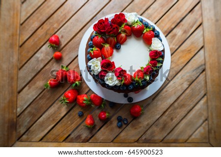 Close up. Delicious Homemade creamy cake with berries and roses. Wood background. 
