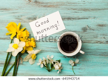 A cup of coffee, spring flowers and the inscription "Good morning" on a wooden background. The concept of the morning, top view.
