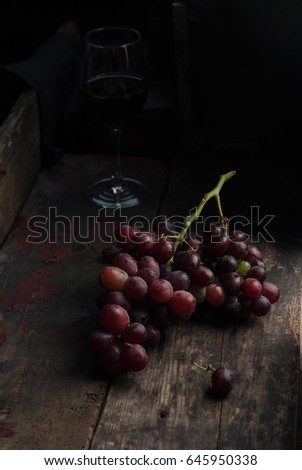 Organic purple grapes and a glass of wine on a dark vintage wooden rustic table. Dark and moody picture. Close up, copy space