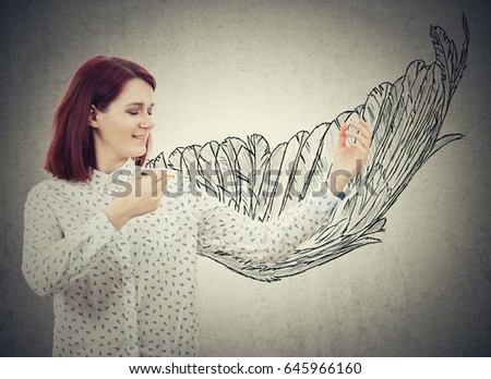 Young smiling businesswoman drawing a wing sketch behind her back. Create super power idea, self development success and freedom concept isolated on grey wall background.