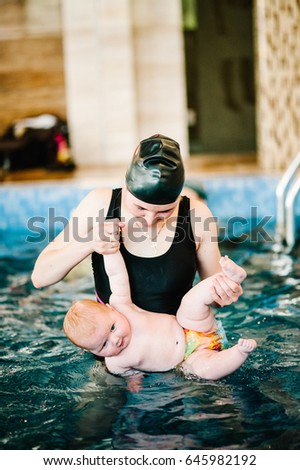 Young mother, swimming instructor and happy little girl in the pool. Teaches infant child to swim. Enjoy the first day of swimming in the water. Mom holds child and do exercises in water. diving.
