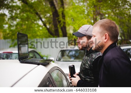 man with a laptop in parking lot in yard near car is doing manipulations with cyber system, concept