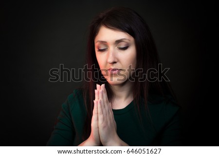 Young woman holding hands together and praying. Studio photography on a dark background.