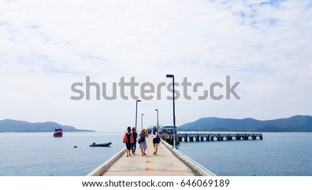 Group of Asian friends walking on concrete pier to go aboard a ship, seascape and mountain background, Group travel concept