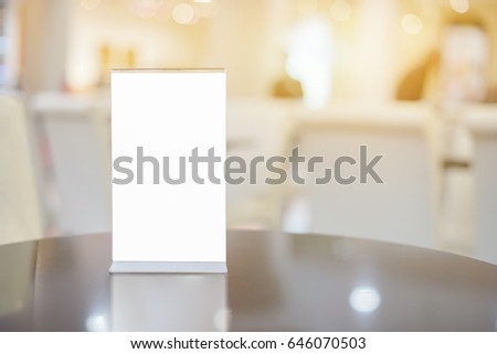 Mock up Menu frame on Table in Bar restaurant ,Stand for booklets with white sheets of paper acrylic tent card on cafeteria blurred ,Chef cooking in background.