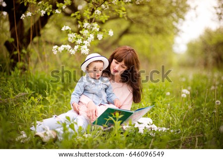 Mother reading a book with tales  to little daughter outdoors in the garden or the park