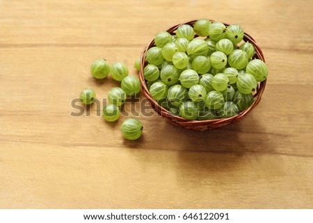 Berry background. Big ripe round green gooseberries in brown wicker small basket on old wooden scratched the surface.