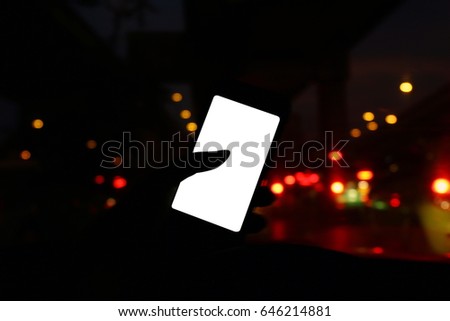 Silhouette in car night with frontal view of modern smart phone and blank white screen empty for copy space for your text or design, Driver and hand using mobile phone bokeh colorful night background