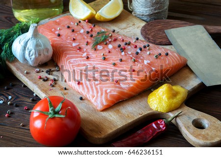 Fresh delicious salmon fillet with aromatic herbs, spices, garlic, lemon on dark background. Top view. Closeup.