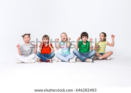 Happy kids. Group of children sit on floor at studio, posing to camera on white isolated background, copy space