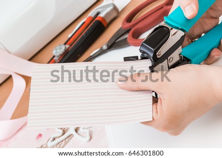 Tools for scrapbooking.oung woman make scrapbook of the papers on the table using tools for cutting paper.