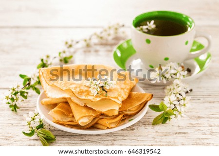 Pancakes, tea and flowers of cherry on a light table. Selective focus.