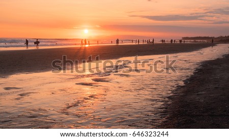 Stunning silhouette of the people on the sandy Echo beach enjoying sunset. Back view of figures of people with surfboards on the coastline. Sun goes down to horizon. Ocean on background. Travel Bali