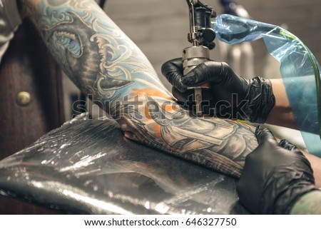 Female master creating tattoo on hand of man with special device in salon. Close up
