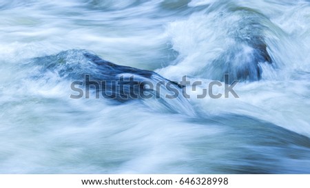 Fast moving water flowing over two boulders. Royalty-Free Stock Photo #646328998