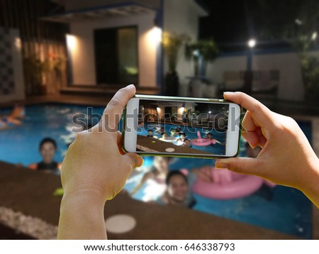 Take a group picture of blurred people on swimming pool background with hand holding smartphone in the fun partty on night