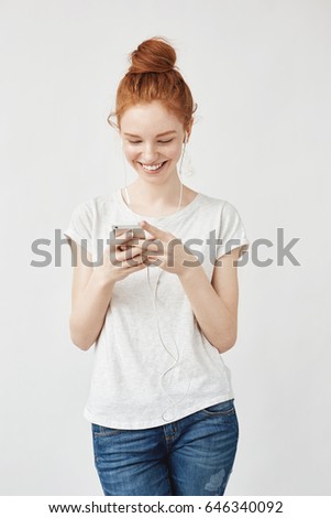 Attractive redhead girl with freckles smiling looking at phone.