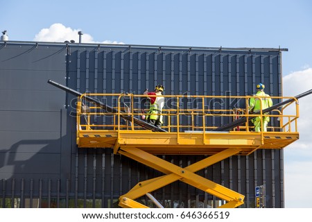 Workers on the aerial work platform at facade installation work Royalty-Free Stock Photo #646366519