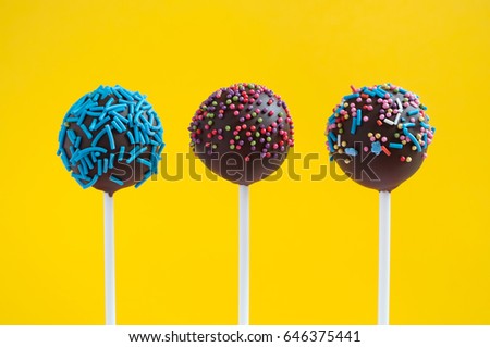 Chocolate cake pops decorated with colorfull confectionery sprinkles on a yellow background. Picture for a menu or a confectionery catalog.
