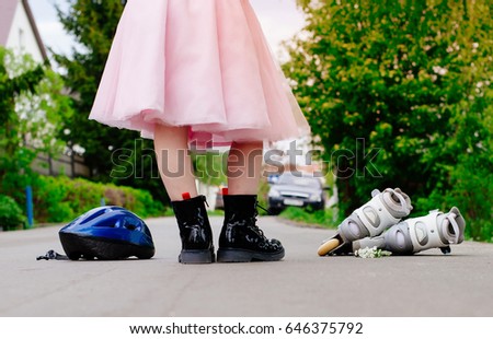 A girl in boots and a pink skirt is standing on the road. The concept of changing  roller skates and activity in an exemplary girl. Audacity and sportiness