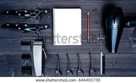 Hairdresser tools on wooden background. Blank card with barber tools flat lay. Top view on wooden table with scissors, comb, clipper and hairdryer with empty notebook and pencil, free space