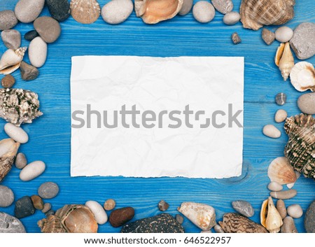 Seashell, pebbles and blank note paper on blue wooden background.